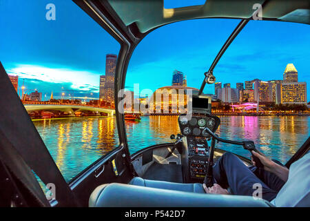 L'intérieur du cockpit de l'hélicoptère voler sur les toits de Singapour à Marina Bay avec les bateaux de croisière dans le port à l'heure bleue. Scène de nuit à bord de la baie de Singapour. Banque D'Images