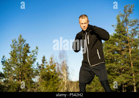 Caucasian Male boxer moyen-âge la formation en dehors de la nature. Belle journée d'hiver ensoleillée dans la forêt avec ciel bleu. Le port de vêtements de sport noir Banque D'Images