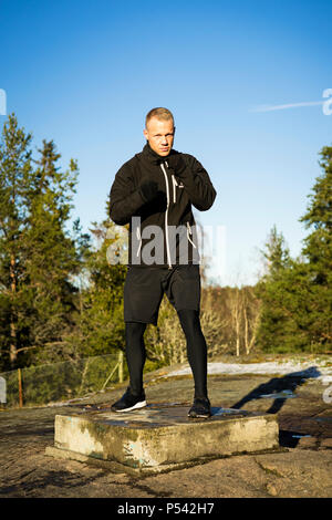 Caucasian Male boxer moyen-âge la formation en dehors de la nature. Belle journée d'hiver ensoleillée dans la forêt avec ciel bleu. Le port de vêtements de sport noir Banque D'Images