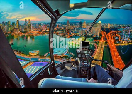 L'intérieur du poste de pilotage d'hélicoptère sur panorama crépusculaire de Singapour Marina Bay avec gratte-ciel lumineux du quartier financier, dans le centre de la ville. Vue aérienne paysage urbain de Singapour. Banque D'Images