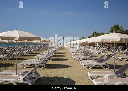 Plage de sable à Mackenzie, Larnaca, Chypre. Chaises longues et parasols à côté de la mer. Ciel bleu en toile de fond, vue rapprochée. Banque D'Images