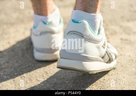 Un homme en blanc chaussures de sport marche sur l'asphalte Banque D'Images