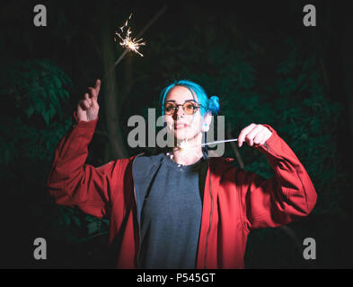 Portrait de jeune fille hippie avec les cheveux teints en bleu avec des baguettes dans les mains et le reflet d'elle dans les verres. Close up belle jeune teenage debout à night city, s'amuser avec le feu de Bengale. Banque D'Images