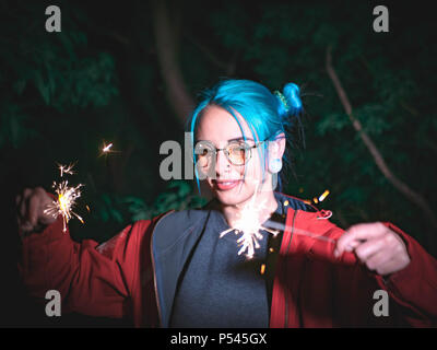 Portrait de jeune fille hippie avec les cheveux teints en bleu avec des baguettes dans les mains et le reflet d'elle dans les verres. Close up belle jeune teenage debout à night city, s'amuser avec le feu de Bengale. Banque D'Images