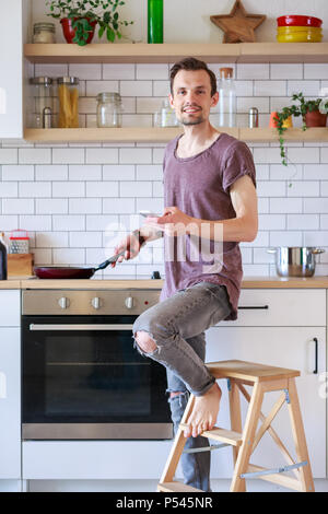 Portrait de brunet homme avec poêle et téléphone dans ses mains dans la cuisine Banque D'Images