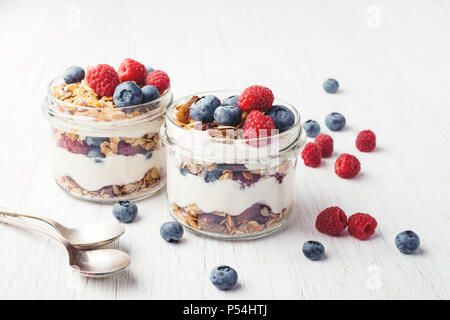 Deux pots de yogourt et petits fruits, granola sur table en bois blanc. Tourné à l'angle. Banque D'Images