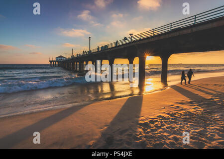 Couple en train de marcher sous le Manhattan Beach Pier au coucher du soleil avec de longues ombres projetées sur la plage, Manhattan Beach, Californie Banque D'Images