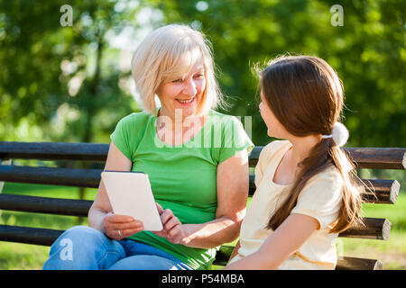 Grand-mère et sa petite-fille sont assis dans un parc et à l'aide de tablette numérique. Banque D'Images