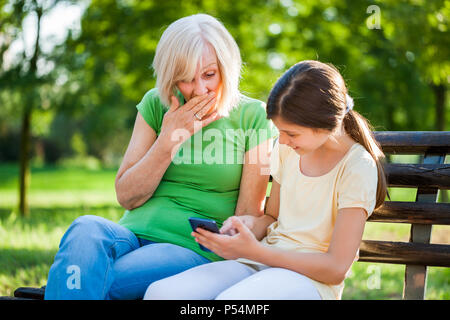 Grand-mère et sa petite-fille sont assis dans un parc et à l'aide de téléphone mobile. Banque D'Images