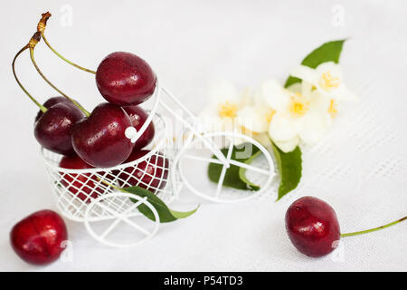 Jouet miniature panier, chariot libre avec cerise mûre, fleurs de jasmin sur un fond clair. Concept d'une alimentation saine, de désintoxication, les vitamines, les régimes Banque D'Images