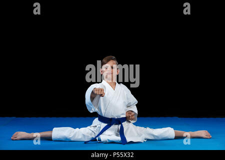 Karaté Kid wearing white gi et la courroie dans un poste de latéral côté split split, Chinois avec les bras croisés sur Banque D'Images