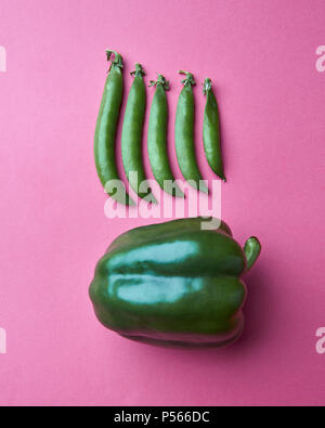 Les gousses de pois vert dans une rangée sur un fond rose avec des poivrons verts, vue du dessus Banque D'Images