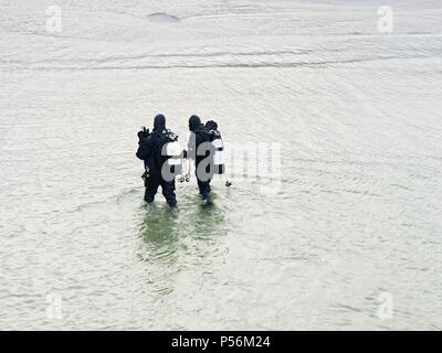 Prerow Allemagne - le 25 janvier 2018 : Deux plongeurs hiver marcher avec leurs engins dans l'eau peu profonde à l'égard de la plage. Banque D'Images