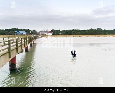 Prerow Allemagne - le 25 janvier 2018 : Deux plongeurs hiver marcher avec leurs engins dans l'eau peu profonde à l'égard de la plage. Banque D'Images