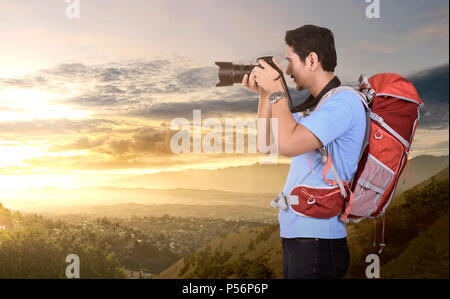 Vue latérale du photographe asiatique homme avec un sac à dos en prenant des photos sur la montagne Banque D'Images