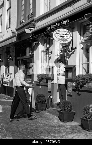 Huidenvettersplein, Brugge, Belgique : chef se tient dans l'embrasure de restaurant Den Gouden Drongen, conversation avec un serveur. Version noir et blanc Banque D'Images