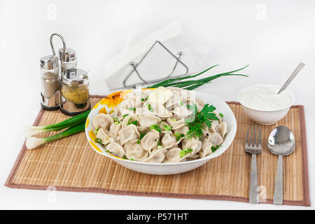 Fédération de quenelles avec les herbes et les oignons. Raviolis de viande. Le plat est servi dans une assiette. Servi avec des boulettes est la crème dans un bol. Banque D'Images