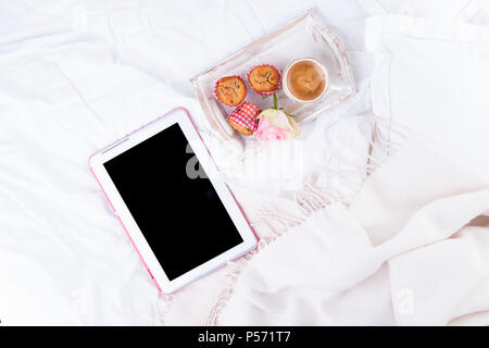 Lit blanc, tablette ordinateur, café frais, petit déjeuner gâteaux et roses roses. Bon matin vintage photo. Copy space Banque D'Images