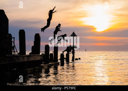 25 juin 2018 . Pays de Galles Aberystwyth UK UK Weather : un groupe de jeunes gens en silhouette sauter dans la mer au large de la jetée sur la plage d'Aberystwyth au crépuscule à la fin d'une autre belle journée de soleil ininterrompues à chaud. Le Royaume-Uni est dans une mini canicule, avec des températures prévues pour frapper 29º ou 30º Celsius par le milieu de la semaine Photo © Keith Morris Crédit : Keith morris/Alamy Live News Banque D'Images