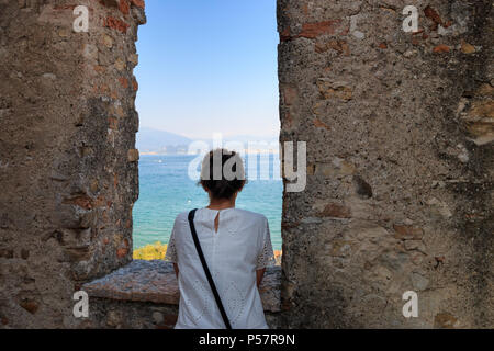 Femme en robe blanche à travers une fenêtre du château scaliger à Sirmione, en Italie, au paysage à Lac de Garde Banque D'Images