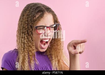 Une adolescente émotionnellement gesticule, fait un doigt sur le côté. Fond studio rose Banque D'Images