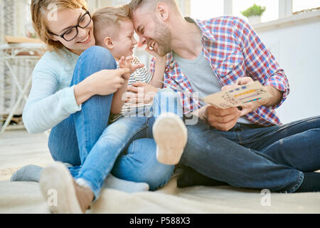 Portrait of happy aux teintes chaleureuses famille aimante jouant avec mignon fils assis sur marbre dans la salle de séjour fête des Pères ensemble Banque D'Images