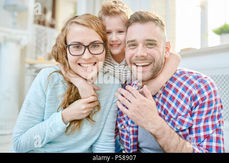 Portrait aux teintes chaleureuses de happy family avec petit fils posing looking at camera à l'intérieur Banque D'Images