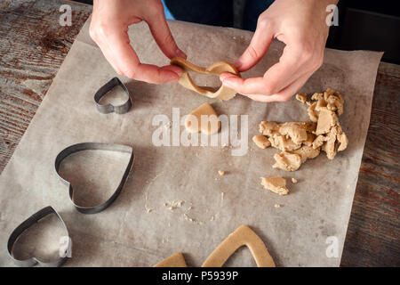 Femme avec ses mains faire des biscuits au gingembre sous forme de cœur sur une table en bois. des gâteaux Banque D'Images