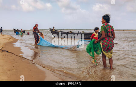 Les femmes rurales avec des filets de pêche en mer avec vue sur les bateaux de pêche en bois à la zone côtière de Kirtania Orissa en Inde. Banque D'Images