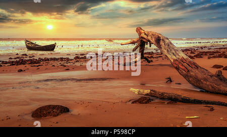 La plage pittoresque de soleil sur la plage près de Digha de Chandpur, Bengale occidental, Inde avec vue sur un tronc d'arbre tombé et bateau de pêche en bois. Banque D'Images