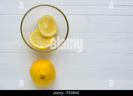 Un citron et deux rondelles de citron dans le verre.la plaque d'un citron est vers le bas et deux rondelles de citron dans la plaque de verre sont sur fond de bois blanc.haut.copie Banque D'Images