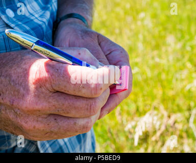 Close up de la main de l'homme écrit avec un stylo pour dater et signer une géocache dans journal de campagne, Ecosse, Royaume-Uni Banque D'Images