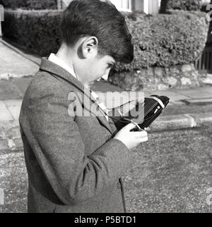 Années 1950, historiques, jeune écolier à l'extérieur de contrôler l'arrière de son appareil photo Kodak Brownie pour voir le nombre de photos qu'il a laissé sur la bobine de film. Banque D'Images