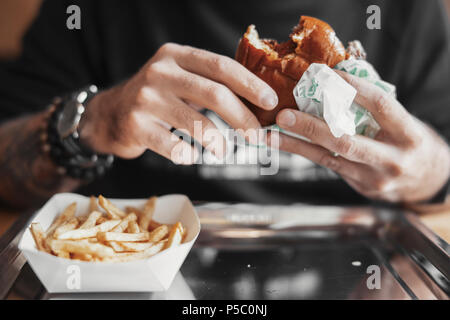 Jeune homme barbu eating hamburger et frites de près. Banque D'Images