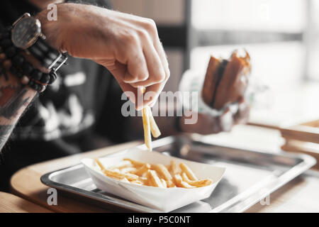Jeune homme barbu eating hamburger et frites de près. Banque D'Images