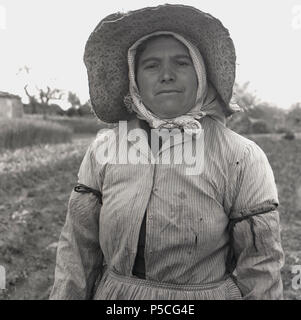 Années 1950, photo by Allan Paiement d'un ouvrier espagnol féminin dans son champ traditionnel Vêtement de travail et portant un grand chapeau de protection, Mallorca. Banque D'Images