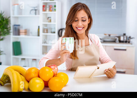 Belle jeune femme est de boire du café et de la lecture recettes dans la cuisine. Banque D'Images