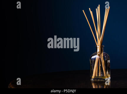 Diffuseurs Reed dans une petite bouteille en verre sur une table avec un fond bleu marine avec l'exemplaire de l'espace sur la gauche Banque D'Images