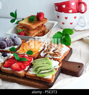 French toasts avec du fromage à pâte molle, fraises, kiwis, noix, cerises et bleuets sur une planche de bois brun, vue du dessus Banque D'Images