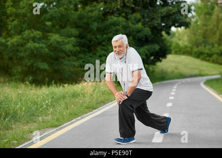 Senior man exercising on l'air frais. Matin, poussant sur le City Park race track. Grand-père ayant corps convenable, mode de vie sain.Wearing white polo, pantalon noir, chaussures de sport. Banque D'Images