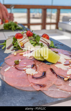 Le carpaccio de boeuf sur une assiette en ardoise avec tomate et fromage parmesan salade. Banque D'Images