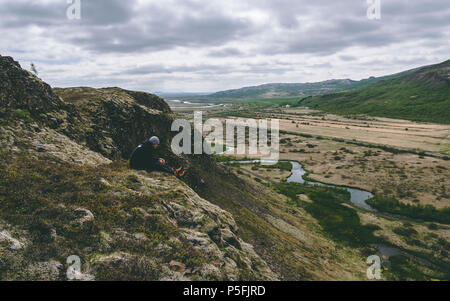 Guy assise sur le bord d'une falaise, à l'islande face non visible Banque D'Images