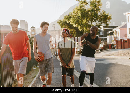 Basket-ball quatre hommes marchant dans la rue parler et avoir du plaisir. Quelques hommes de retour après un match de basket-ball. Banque D'Images