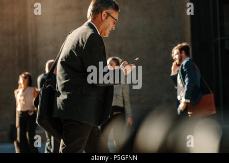 Les gens d'affaires pressés d'atteindre à l'aide de bureau téléphone mobile en marchant sur la rue de la ville. Les hommes et les femmes se rendre au bureau le matin l'exécution de Banque D'Images