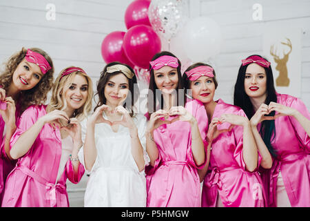 De belles demoiselles en robe rose et masques de sommeil avec bride montrant l'amour signe avec les mains. Banque D'Images