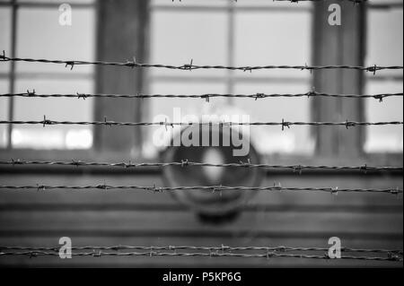 Close up du fil barbelé contre l'arrière-plan flou avec Spotlight et windows sur un bâtiment. Noir et blanc - camp de concentration d'Auschwitz Banque D'Images