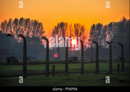 Coucher du soleil jette une lueur orange au camp de concentration d'Auschwitz-Birkenau. Une clôture en fil barbelé se sépare d'un paysage magnifique et d'un sombre passé Banque D'Images