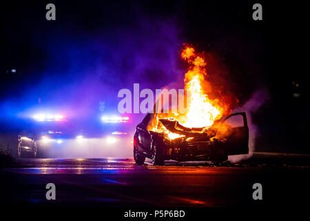 Voiture en feu dans la nuit avec les lumières de police en arrière-plan dans la nuit Banque D'Images