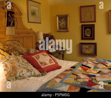 Coussins floraux et d'arlequin sur pin antique lit dans chambre pays jaune Banque D'Images