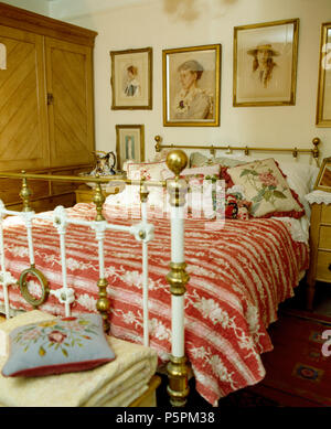 Vintage photos sur mur au-dessus de lit en laiton victorien avec red +couette et coussins blancs floraux en chambre cottage Banque D'Images